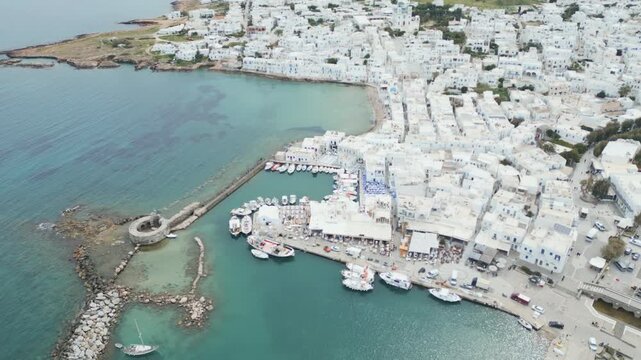 Aerial drone view of Naousa village on Paros island, Greece, showing traditional white buildings, coastal harbor and clear blue sea in daylight. Ideal for travel, tourism and Mediterranean lifestyle 
