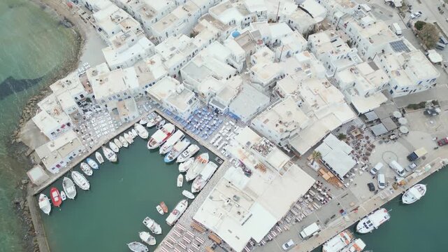 Aerial drone view of Naousa village on Paros island, Greece, showing traditional white buildings, coastal harbor and clear blue sea in daylight. Ideal for travel, tourism and Mediterranean lifestyle 