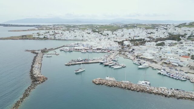 Aerial drone view of Naousa village on Paros island, Greece, showing traditional white buildings, coastal harbor and clear blue sea in daylight. Ideal for travel, tourism and Mediterranean lifestyle 