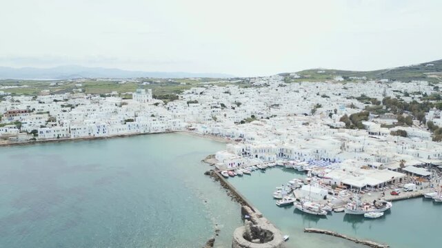 Aerial drone view of Naousa village on Paros island, Greece, showing traditional white buildings, coastal harbor and clear blue sea in daylight. Ideal for travel, tourism and Mediterranean lifestyle 