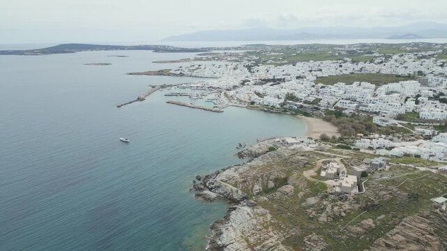 Aerial drone view of Naousa village on Paros island, Greece, showing traditional white buildings, coastal harbor and clear blue sea in daylight. Ideal for travel, tourism and Mediterranean lifestyle 