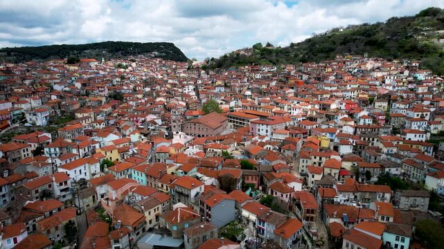 4K aerial drone footage over Agiasos village in Lesvos at midday, featuring dense tile rooftops, traditional architecture, and a soft overcast sky with white clouds enhancing the authentic atmosphere.