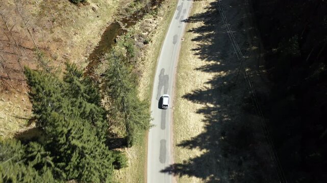 Drone tracking car on winding forest road, aerial travel shot