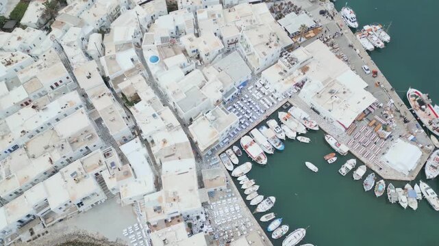 Aerial drone view of Naousa village on Paros island, Greece, showing traditional white buildings, coastal harbor and clear blue sea in daylight. Ideal for travel, tourism and Mediterranean lifestyle 