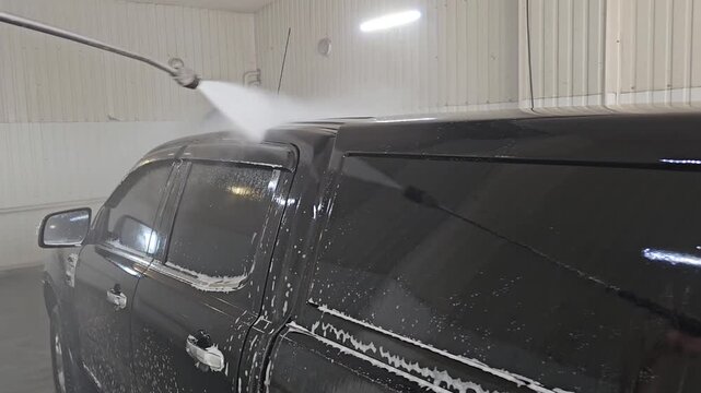 Black 4x4 off-road being washed with foam and water, generic full-size vehicle cleaning, all-wheel drive car exterior detailing with suds and spray at car wash, no visible brand