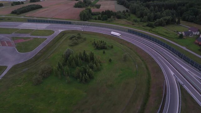 Aerial shot of curved highway exit ramp and multilane road junction. Modern transport infrastructure surrounded by green fields.