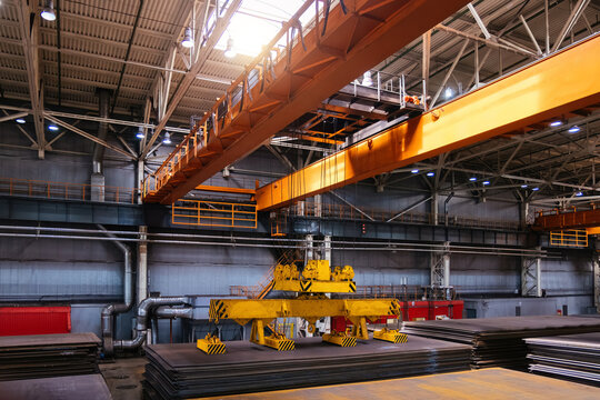 Overhead crane with magnetic grippers lifting steel sheets in metalworking factory warehouse