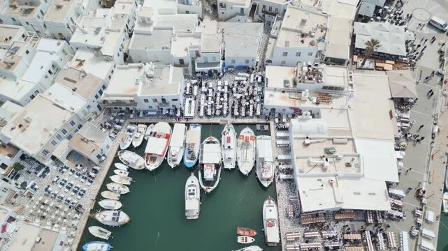 Aerial drone view of Easter celebration in Naousa village on Paros island, Greece, showing people gathered at outdoor tables in a festive Mediterranean atmosphere. Ideal for culture, travel, holidays