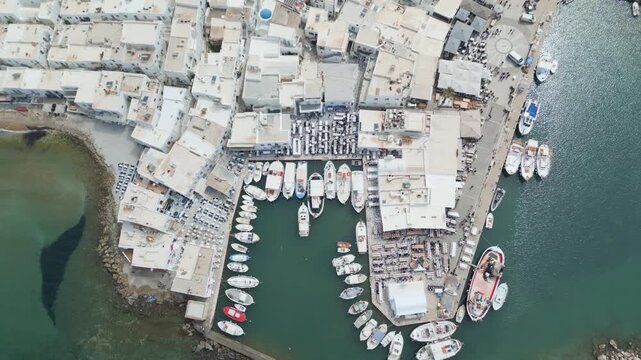 Aerial drone view of Naousa village on Paros island, Greece, showing traditional white buildings, coastal harbor and clear blue sea in daylight. Ideal for travel, tourism and Mediterranean lifestyle 