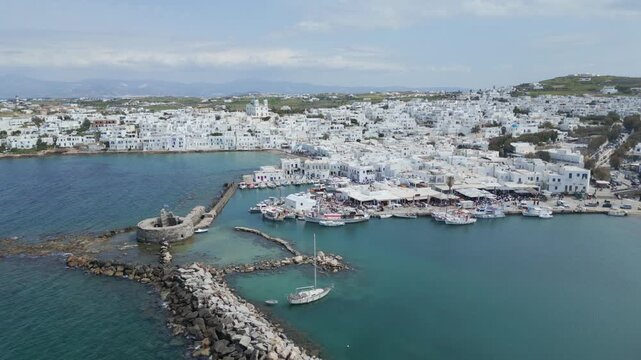 Aerial drone view of Naousa village on Paros island, Greece, showing traditional white buildings, coastal harbor and clear blue sea in daylight. Ideal for travel, tourism and Mediterranean lifestyle 