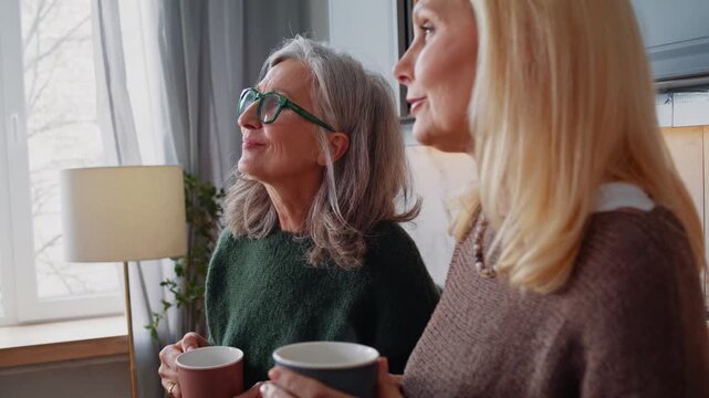 Happy old women talk and drink tasty tea spending time in kitchen