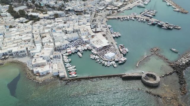 Aerial drone view of Naousa village on Paros island, Greece, showing traditional white buildings, coastal harbor and clear blue sea in daylight. Ideal for travel, tourism and Mediterranean lifestyle 