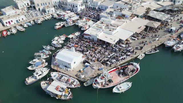 Aerial drone view of Easter celebration in Naousa village on Paros island, Greece, showing people gathered at outdoor tables in a festive Mediterranean atmosphere. Ideal for culture, travel, holidays