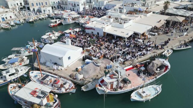 Aerial drone view of Easter celebration in Naousa village on Paros island, Greece, showing people gathered at outdoor tables in a festive Mediterranean atmosphere. Ideal for culture, travel, holidays