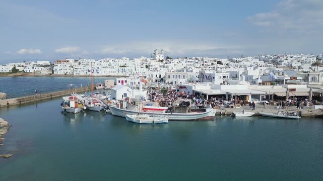 Aerial drone view of Easter celebration in Naousa village on Paros island, Greece, showing people gathered at outdoor tables in a festive Mediterranean atmosphere. Ideal for culture, travel, holidays