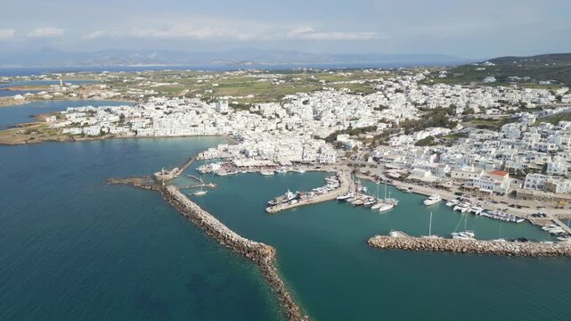 Aerial drone view of Naousa village on Paros island, Greece, showing traditional white buildings, coastal harbor and clear blue sea in daylight. Ideal for travel, tourism and Mediterranean lifestyle 
