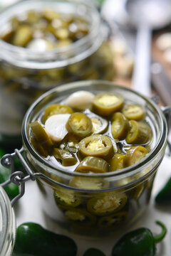 Close up of jar filled with pickled jalapeno slices in brine. Preserved green chili texture with seeds and liquid