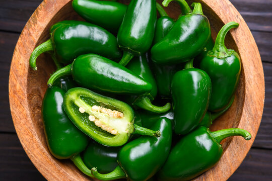 Close up of jalapeno peppers in wooden bowl with one sliced piece. Fresh green chili seeds visible natural food detail