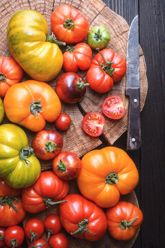 Bright heirloom tomatoes arranged on round cutting board. Rustic kitchen styling, vegetarian healthy ingredients