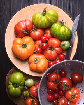 Assorted heirloom tomatoes in wooden bowls and plate, top view. Colorful organic harvest, farm to table concept