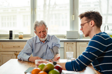 Fototapeta premium Grandson helping senior grandfather monitoring blood pressure at home