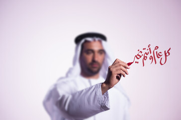 Obraz premium Emirati man writing Happy New Year greeting in Arabic calligraphy with red marker