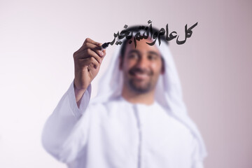 Obraz premium Man in traditional white robe writing Arabic New Year greeting on glass with a marker