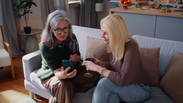 Happy mature woman shows boyfriend photo on smartphone to friend