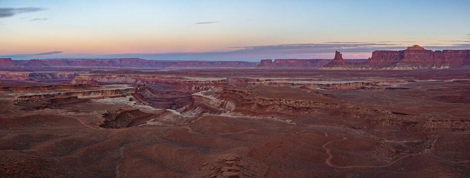 This scenic Canyonlands National Park panorama at dawn features the White Rim Road winding its way around Green River Canyon under a colorful sky.