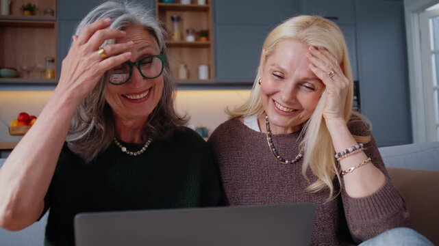 Senior women laugh together while watching laptop on sofa