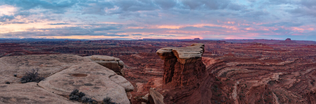 This scenic sunrise panorama of Canyonlands National Park features a lone tower near White Crack underneath a colorful sky.