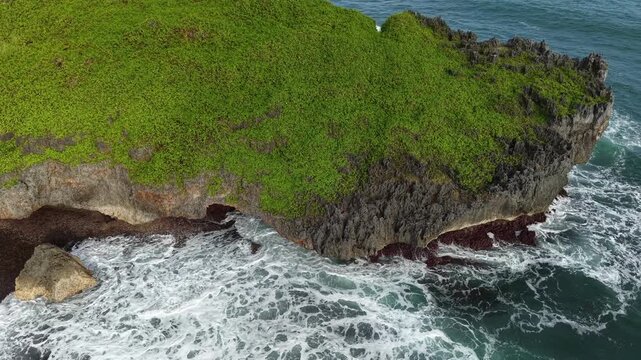 Natural formation of a green-topped rock surrounded by deep blue ocean currents.