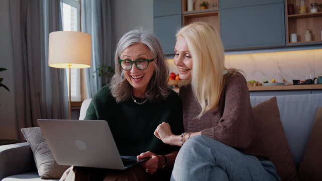 Pair of senior women shares laptop content smiling on sofa