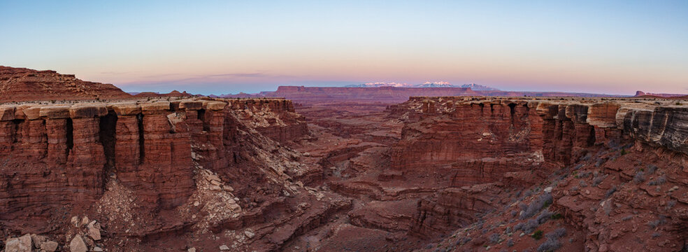 This scenic sunset panorama of Canyonlands National Park features Gooseberry Canyon with the snow-capped La Sal Mountains in the distance underneath a colorful sky.
