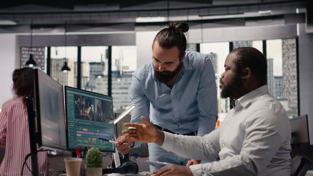 Videographers editing video footage on computer in creative agency, process of cutting and adjusting color grading on software with sliders. Diverse team working in movie post production.