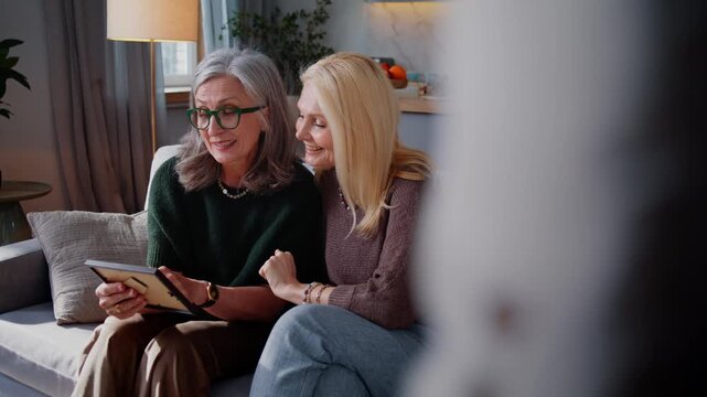 Mature women look at framed photo together and smile on sofa