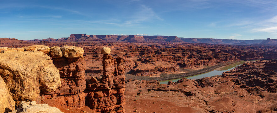 This panorama of Canyonlands National Park features the Colorado River with a unique rock pinnacle along the rim of this eroded canyon.