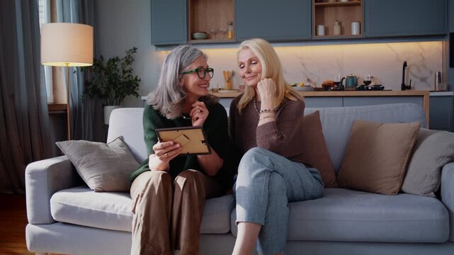 Elderly women look at old photo together smiling on sofa