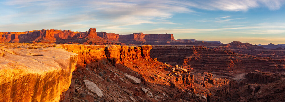 This scenic sunrise panorama from within Canyonlands National Park near Moab, Utah, features the sun's soft light at sunrise illuminating the inner canyon rim.