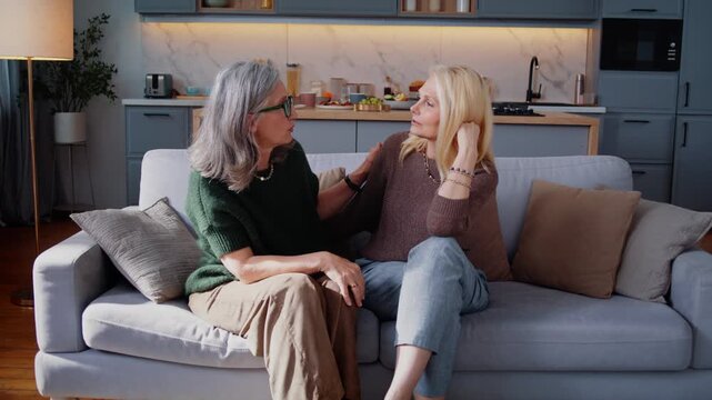 Elderly women hug talking with joyful smiles on sofa at home