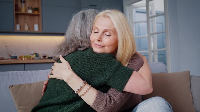Senior women share warm embrace on sofa during reunion home