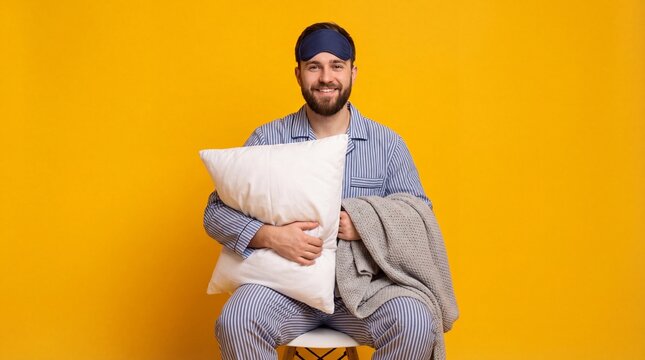 Man in striped pajamas and eye mask holding a pillow and blanket against a vibrant yellow background