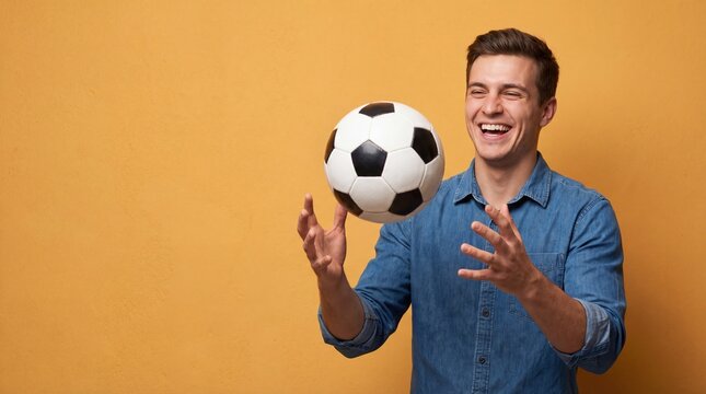 Young man gleefully playing with a soccer ball against a vibrant orange background enjoying leisure