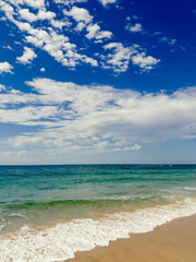 Fototapeta premium Ocean waves washing up to a sandy beach under a blue sky with light white clouds