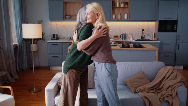 Mature women stand hugging during happy friends reunion at home