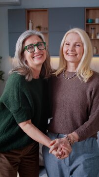Elderly women hold hands smiling in warm home moment together