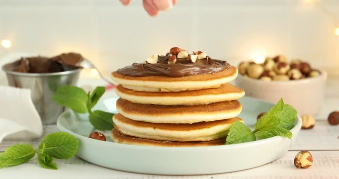 Woman adding mint to tasty pancakes with chocolate paste at light wooden table, closeup