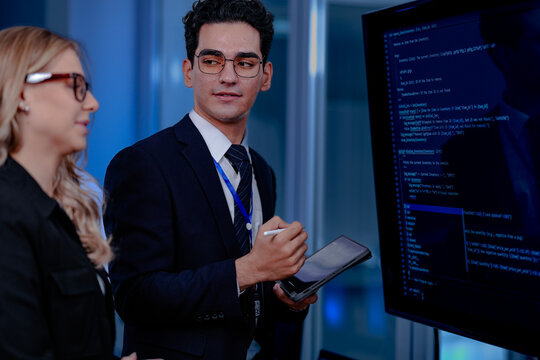 Code breakthrough achieved. Smiling senior developer points to a successful code segment on screen, sharing the solution with his colleague during a late night pair programming session.