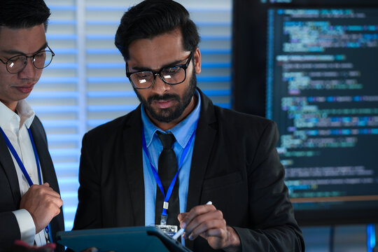 AI research team huddles late night innovators review complex machine learning model architecture discuss training data using tablet stylus futuristic lab code screens glow bright.