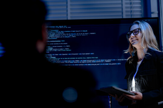 A female software architect presents the system architecture or walks through a complex codebase on a large screen using a tablet to guide her development team during a review.